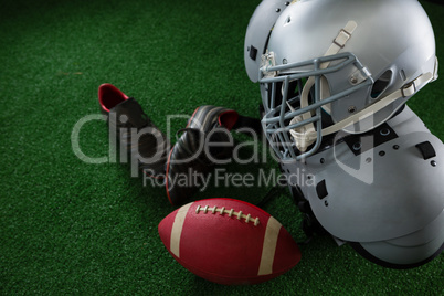 American football shoulder pads, head gear, football and cleats over artificial turf