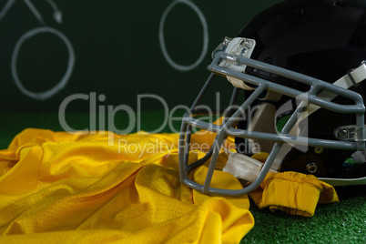 American football jersey and head gear lying on artificial turf against strategy board
