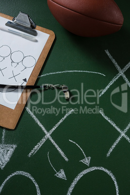 American football and referee whistle lying on green board with strategy drawn on it