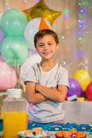 Cute boy standing with arms crossed at birthday party