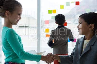 Businesswomen shaking hands while businessman standing in background