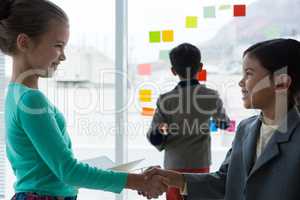 Businesswomen shaking hands while businessman standing in background