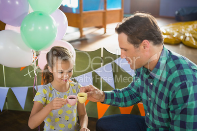 Father and girl toasting their tea cups while playing with toy kitchen set