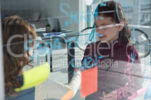 Female coworkers discussing by window seen through glass