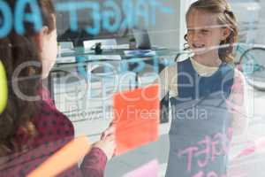 Female coworkers giving handshake at office seen through glass