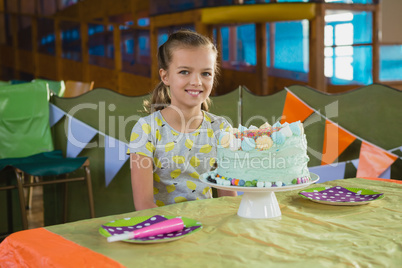 Girl sitting near a birthday cake at home