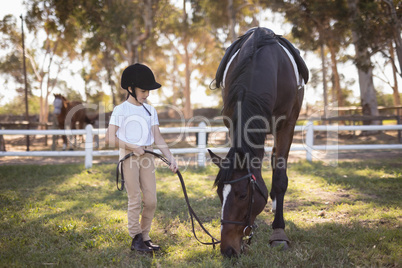 Full length of girl wearing helmet standing by horse