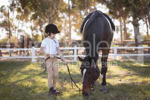 Full length of girl wearing helmet standing by horse