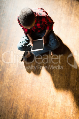 Boy sitting on wooden floor using digital tablet