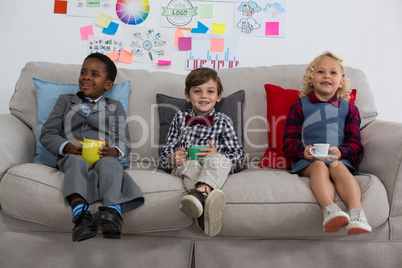 Portrait of business people having drink while relaxing on sofa in office