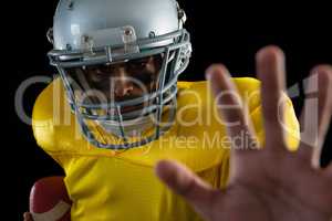 American football player holding a ball and gesturing a hand stop sign