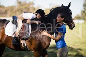 Female jockey and girl embracing horse