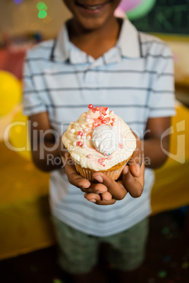 Boy holding decorated cupcake during birthday