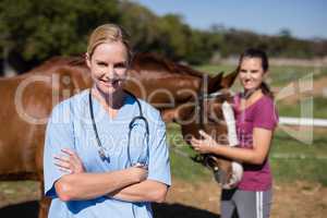 Portrait of female vet with woman standing by horse in background