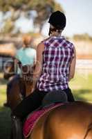 Rear view of woman horseback riding with friend sitting on horse in background