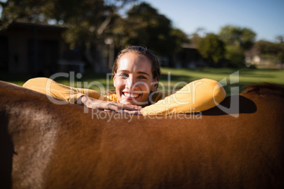 Happy female jockey leaning on horse at barn