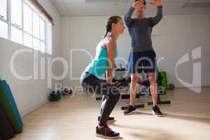 Trainer training woman in lifting kettlebells at fitness studio