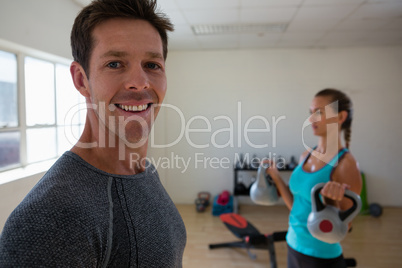 Portrait of male trainer standing by athlete lifting kettlebells