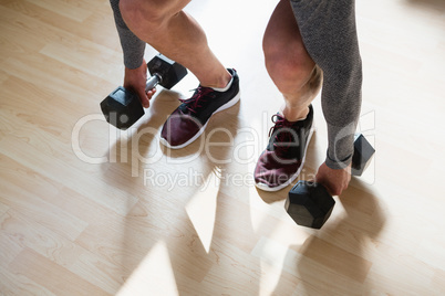 Low section of athlete lifting dumbbells in gym