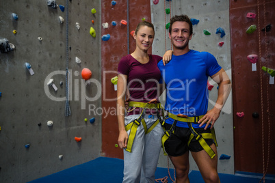 Portrait of male trainer with female athlete standing by climbing wall