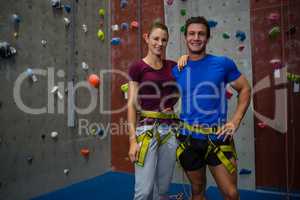 Portrait of male trainer with female athlete standing by climbing wall