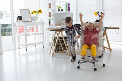 Cheerful male colleagues pushing businesswoman sitting on chair in office