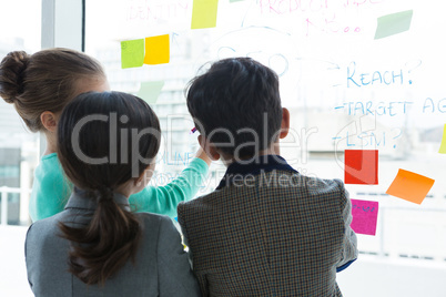 Rear view of business people discussing while writing on window