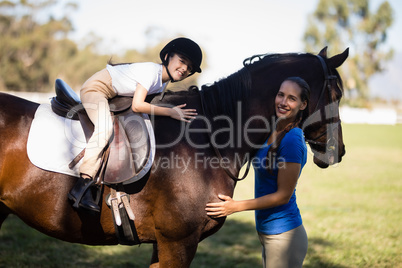 Portrait of smiling jockey and girl embracing horse