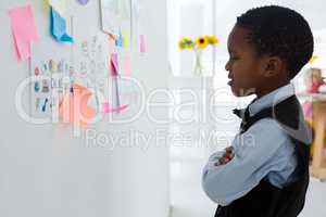 Businessman with arms crossed looking at adhesive notes on whiteboard in office