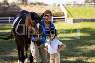 Happy female jockey with sister standing by horse
