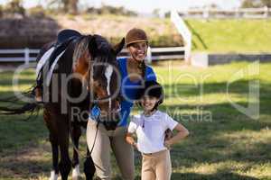 Happy female jockey with sister standing by horse