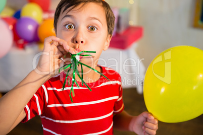 Cute boy blowing party horn during birthday party
