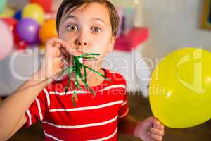 Cute boy blowing party horn during birthday party