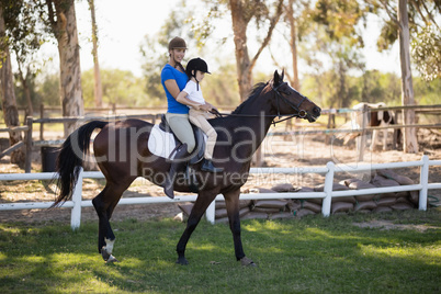 Side view of female jockey teaching horseback riding to girl