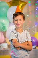 Cute boy standing with arms crossed at birthday party