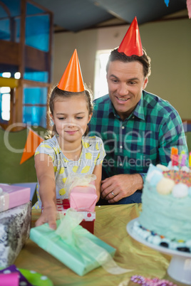 Smiling father and daughter in party hat looking gift box