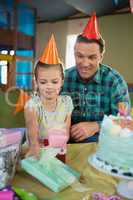 Smiling father and daughter in party hat looking gift box