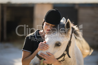 Female jockey embracing horse at barn