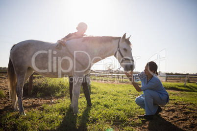 Woman looking at vet examining horse in barn