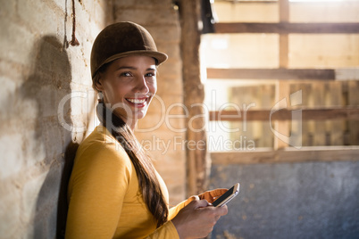 Portrait of smiling female jockey using mobile phone in stable