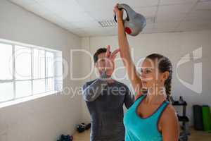 Male trainer assisting female athlete in lifting kettlebells