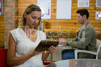 Young woman with tablet while young man using laptop in background