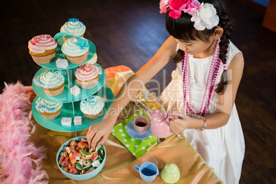 Girl having tea and confectionery at table during birthday party