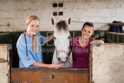 Portrait of smiling female vet with woman standing by horse