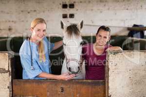 Portrait of smiling female vet with woman standing by horse