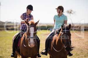 Full length happy female friends talking while horseback riding
