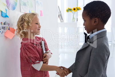 Business people giving handshake while standing by whiteboard in office