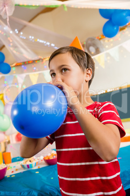 Cute boy blowing balloon during birthday party