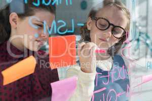 Businesswoman looking at female colleague writing on window