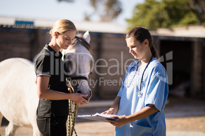 Female vet showing reports to jockey standing by horse
